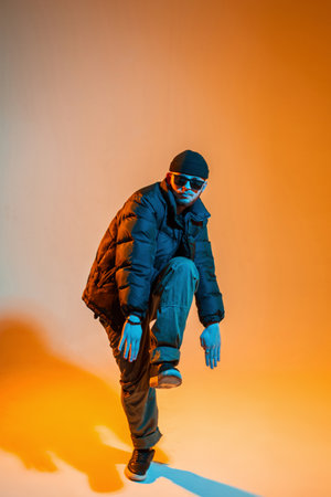 Stylish professional dancer guy in fashion black clothes with a hat, sunglasses, a down jacket,...