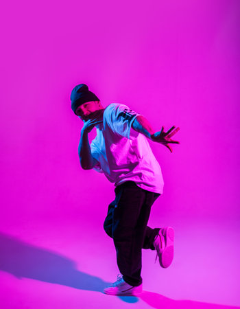 Handsome professional break dancer guy in trendy fashion clothes dancing in creative studio with pink and neon lightの写真素材