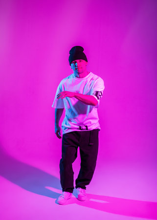 Handsome hip hop b-boy dancer in fashion clothes with a hat dancing in a color studio with pink and...