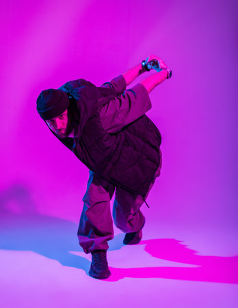 Stylish dancer guy in trendy clothes dancing in a creative color studio with pink and neon lightsの写真素材