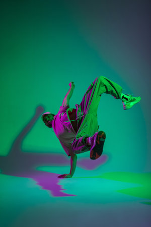 Fashionable professional hip hop dancer man b-boy in fashion trendy clothes with a cap and stylish sneakers dances on his hands in a creative color studio with cyan and magenta lightの写真素材