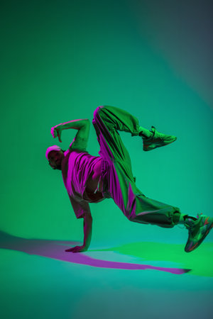 Stylish professional dancer guy hip hop b-boy in fashionable clothes with a cap and sneakers dances on hand in a creative studio with magenta and cyan colorの写真素材