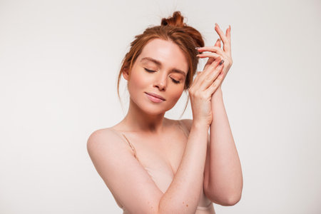 Beautiful tender young fresh girl model with red hair does hand and skin care on a white background in the studio. Beauty, health and skin careの写真素材