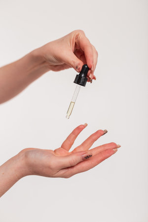 Female hands holding drops of cosmetics oil with a pipette and doing hand skin care, close-up. Beauty and health, skin careの写真素材
