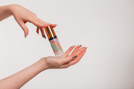 Young red-haired girl holds cosmetics makeup base in hands a on a white background. Beauty, cosmetics and skin careの写真素材