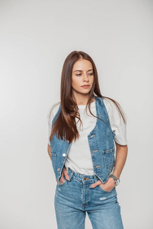 Stylish beautiful fashion woman model in fashionable denim clothes with a denim vest, t-shirt and jeans on a white backgroundの写真素材
