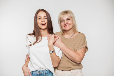Beautiful young happy daughter and a lovely elderly mother with a smile in a fashionable t-shirt on a white background in the studioの写真素材