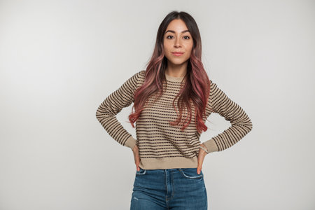 Pretty young woman model with freckles and pink hair in fashion clothes with a sweater stands on a white background in the studioの写真素材