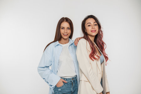 Two beautiful young girlfriend model girls with a smile in fashionable denim casual clothes on a white background in the studioの写真素材