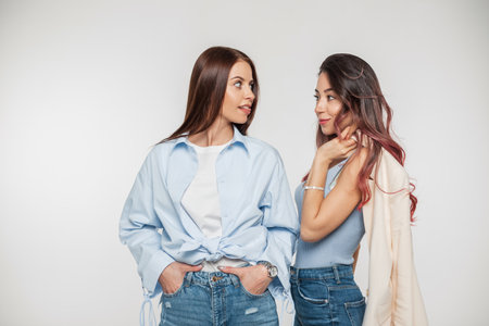 Two funny beautiful young girlfriends in fashionable casual clothes show their tongue and fool around on a white backgroundの写真素材