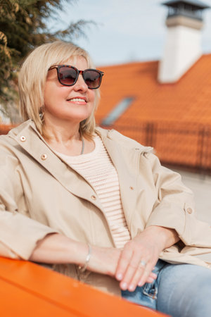 Successful beautiful mature business lady with smile with stylish sunglasses in trendy fashion casual beige clothes sits and rests on a sunny spring dayの写真素材