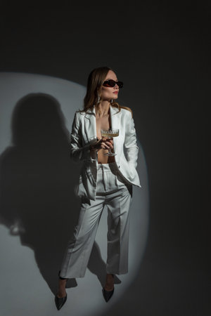 Elegant beautiful lady with sunglasses in a fashion white suit with a vintage glass of champagne at a partyの写真素材