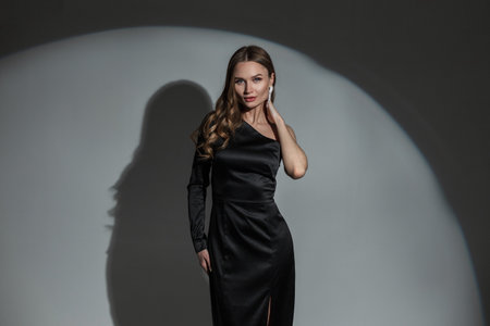 Gorgeous beautiful chic lady with a diamond earring in a trendy fashion black elegant dress posing on a dark background with a round light in studio. Pretty woman celebrating an eventの写真素材