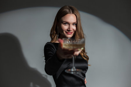 Happy beautiful chic woman with a smile in a fashionable elegant black dress holding a vintage glass of champagne at a party. Pretty lady celebrationの写真素材