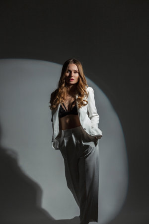 Sexy glamorous beautiful fashion woman in stylish elegant white suit with bra posing on dark background in studioの写真素材