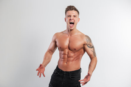 Strong athlete handsome man with emotions with muscular body screaming on a white background in the studioの写真素材