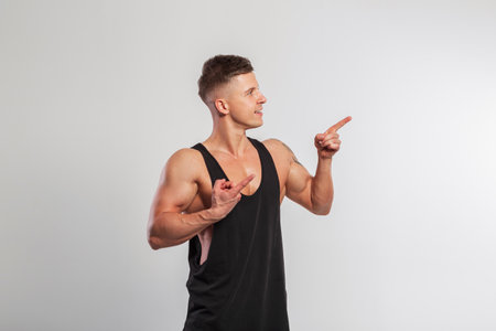Handsome muscular athletic man with hairstyle and black t-shirt pointing with fingers at free space for design and product on white backgroundの写真素材