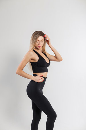 Beautiful young woman fit model with a slender body in fashionable black sportswear with a top and leggings posing on a white backgroundの写真素材
