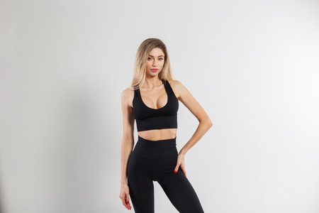 Beautiful blonde athletic fitness lady in sports fashionable black clothes with a top and leggings on a white backgroundの写真素材