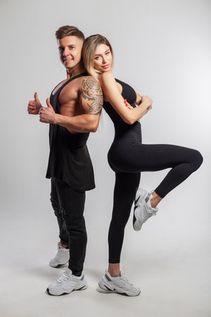 Beautiful happy sports couple posing in the studio on a white background. Beautiful slim fitness girl and muscular handsome man in black sportswear with sneakersの写真素材