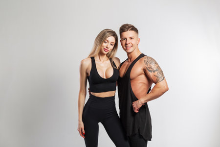 Beautiful sports couple in the studio. Beautiful young fitness girl and handsome strong muscular man in fashionable black sportswear on a white backgroundの写真素材
