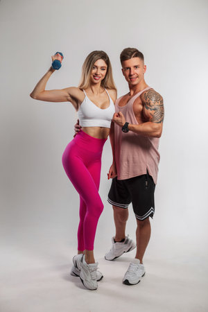 Beautiful fashionable sports couple posing on a white background. Beautiful fitness girl and handsome muscular man trainer in sportswear with sneakers in the studioの写真素材