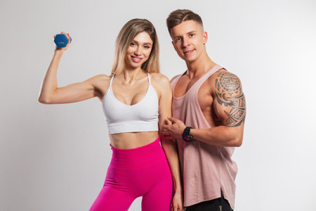 Beautiful sportswear fitness couple on a white background. Pretty happy fit girl holding a dumbbell and a handsome muscular manの写真素材