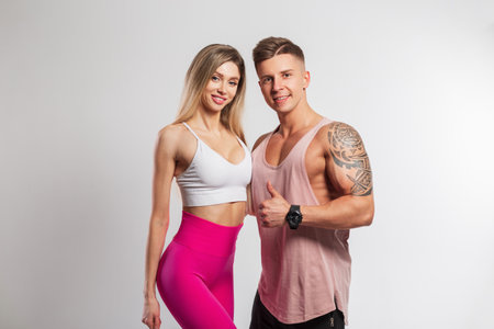 Beautiful healthy happy fitness couple on a white background. Beautiful fitness lady with smile and handsome muscular guy in sportswear in the studioの写真素材