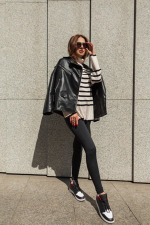 Fashionable beautiful young girl model in stylish clothes with a trendy leather jacket, striped...
