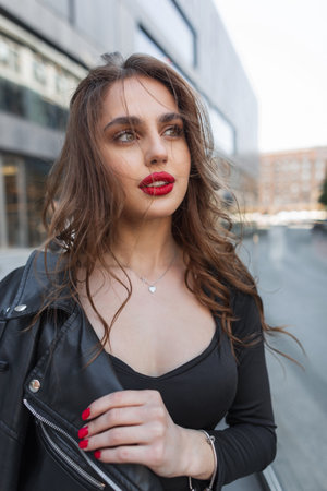 Street female portrait of a beautiful fashionable chic girl with red lips in fashion black clothes with a leather jacket walks in the cityの写真素材