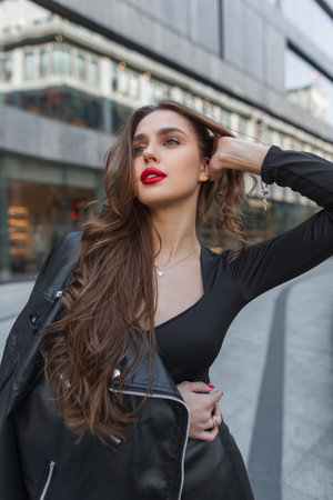 Fashionable beautiful stylish chic girl with red lips in fashion elegant clothes with a leather jacket walks in the cityの写真素材