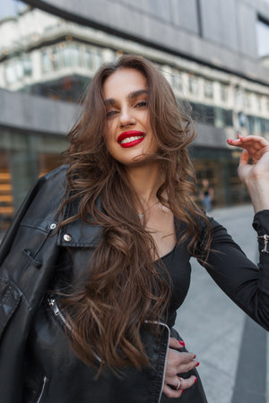 Happiness beautiful young stylish chic woman with smile and red lips in casual fashion outfit with leather jacket walks in the cityの写真素材