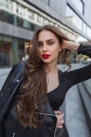 Fashionable young glamor pretty chic lady with red lips in black stylish clothes with leather jacket walks in the cityの写真素材