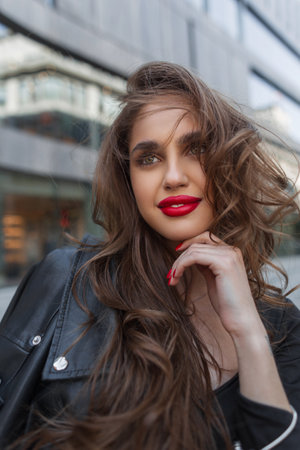 Female street portrait of beauty happy young chic fashionable woman with red lips in black clothes with leather jacket walks in the cityの写真素材