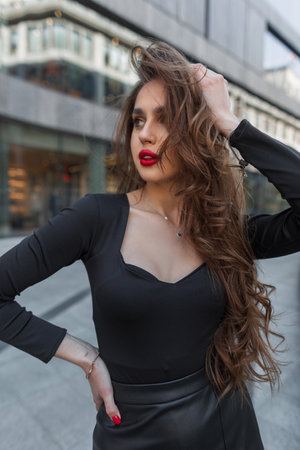 Gorgeous beautiful fashion brunette girl with red lips in elegant clothes walks in the city and straightens her hairの写真素材