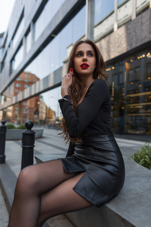 Beautiful fashionable stylish elegant woman with red lips with sexy legs in a casual skirt sits in the cityの写真素材