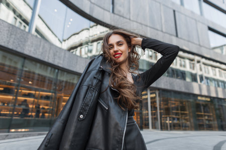 Beautiful happy fashion woman with red lips in trendy stylish clothes with black leather jacket walking and poses in the cityの写真素材