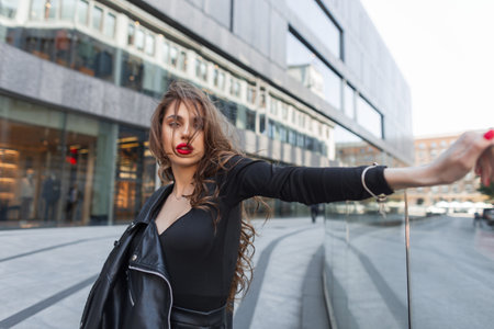 Beautiful elegant beautiful young gorgeous stylish chic woman with red lips in fashion black clothes walks and poses in the city near the modern mallの写真素材
