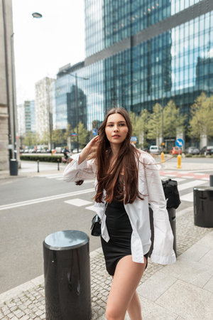 Stylish beautiful street young girl in fashion clothes with a white shirt and black dress walks in the cityの写真素材
