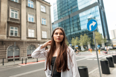 Stylish beautiful young woman model in fashion clothes with a white shirt and black dress walks in the cityの写真素材