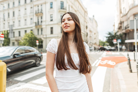 Beautiful street fashion woman in stylish white dress walks in the city on a sunny dayの写真素材