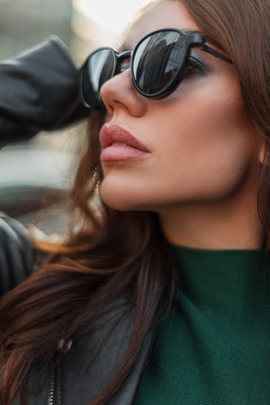 Close-up fashion female portrait of a beautiful stylish cool woman with clean face skin and sexy lips in trendy stylish clothes with fashion black sunglasses in the cityの写真素材