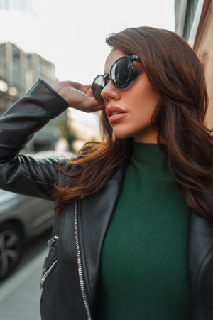 Beautiful fashion stylish fresh woman model in trendy street clothes with leather jacket with fashionable black sunglasses walks in the cityの写真素材