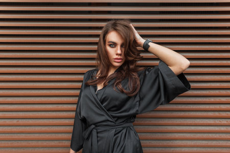 Styling beauty young stylish chic lady with brunette hairstyle in a fashion elegant black suit stands near a rusty metal wall in the cityの写真素材