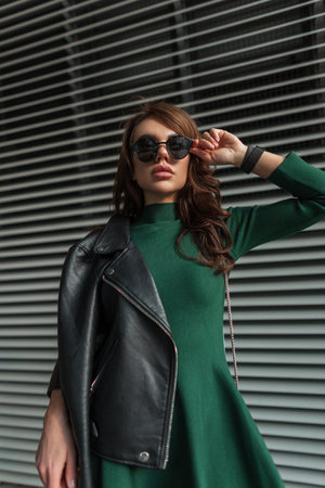 Cool trendy stylish woman model in fashionable urban outfit with green dress with leather jacket wears trendy sunglasses on the streetの写真素材