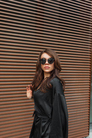 Beautiful trendy chic girl with cool sunglasses in a fashion black suit near a metal rust wall walks on the streetの写真素材