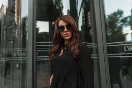Fashion beauty woman model with vintage sunglasses in trendy black fashionable clothes with dress walks in the city. cool pretty womanの写真素材