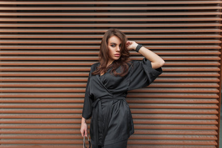 Fashionable pretty lady with makeup in elegant fashion black dress stands near a rusty metal lines background on the streetの写真素材