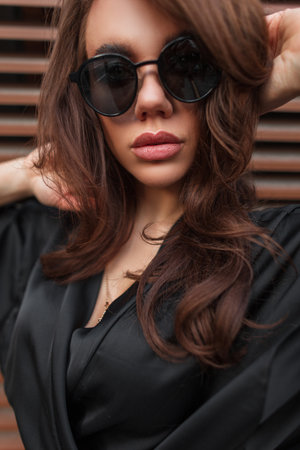 Glamor female portrait of beautiful young woman brunette model with fashion sunglasses in elegant dress poses on the streetの写真素材