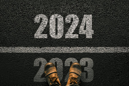 Man walks on asphalt and crosses the line by 2024. New year 2024. Men's legs with leather shoes go to 2024. End of 2023 and beginning of 2024の写真素材